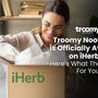 woman smiling opening a cardboard box that says "iHerb" in green text