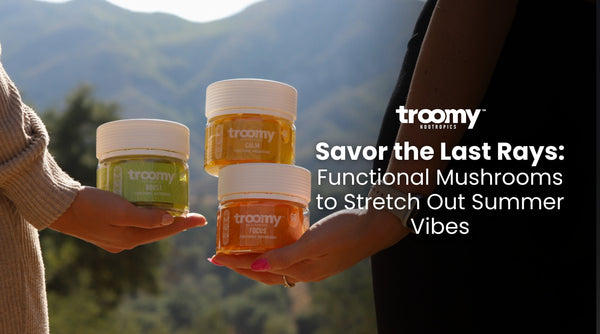 two women holding adaptogenic mushroom jars outdoors with the sun shining on the products big green mountains in the background