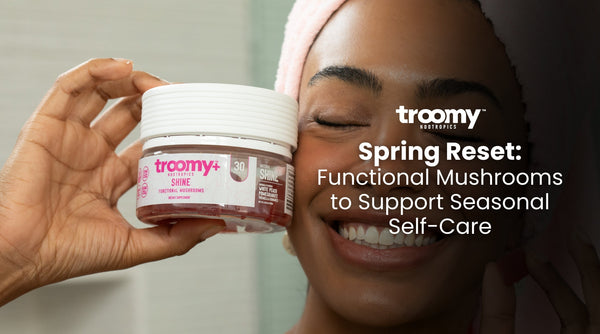 woman in pink bath towel holding up a collagen gummy supplement next to clear shiny skin